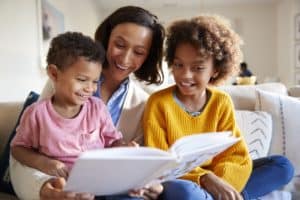 Mother sitting on sofa in the living room with her children, reading them a book
