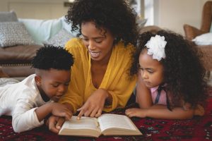 Mother with her cute children lying on floor and reading a book in a comfortable home Mother with her cute children lying on floor and reading a book in a comfortable home